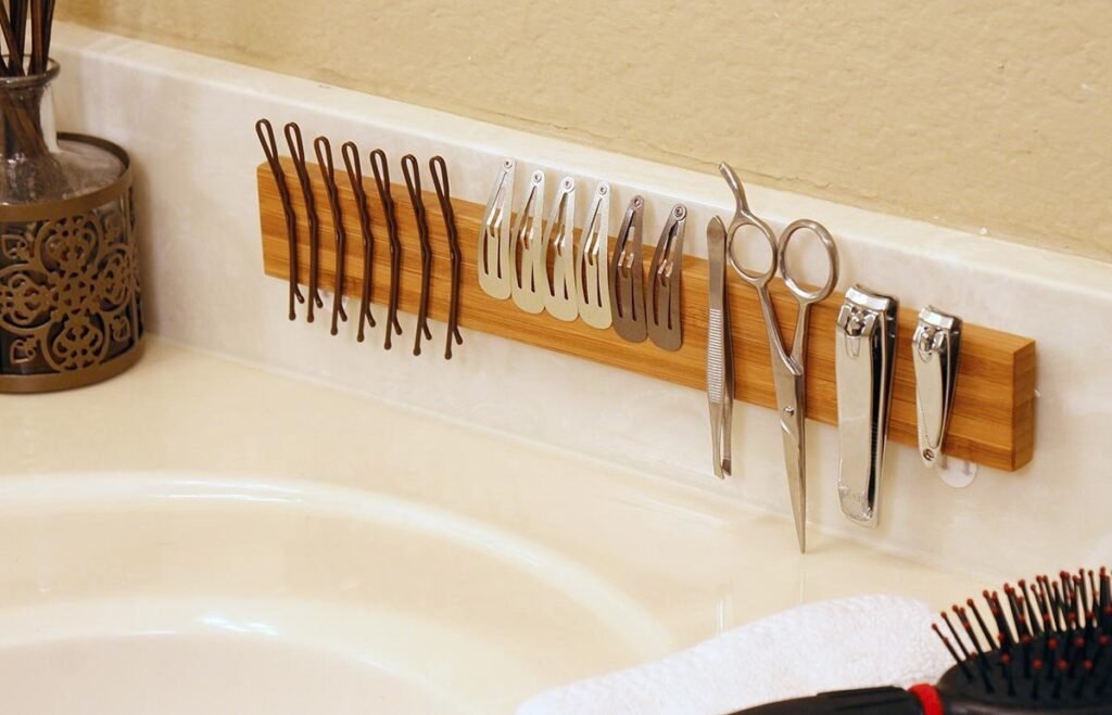 Magnetic strip mounted on a bathroom wall organizing small metal essentials like tweezers, scissors, and razors.