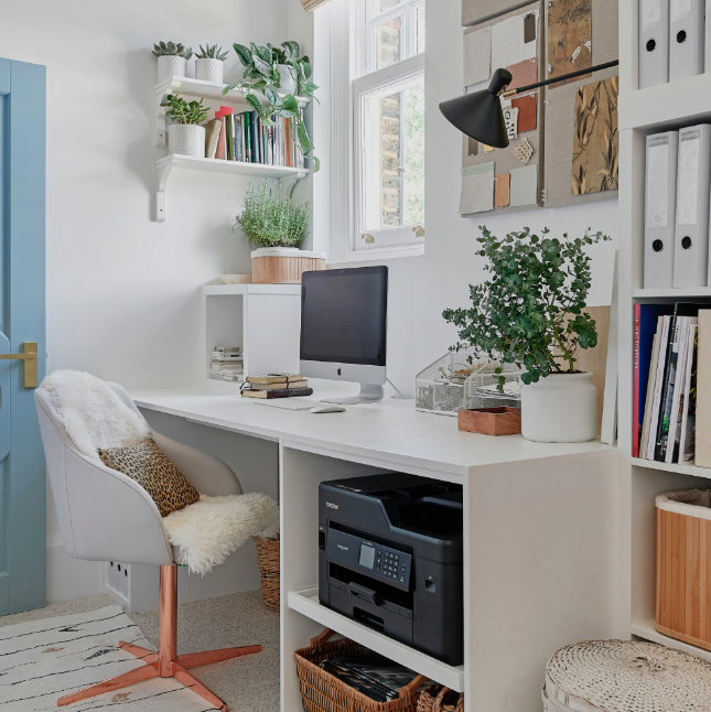 Compact white built-in home office desk with shelves and printer storage, styled with plants and files; bright small-room workspace near a window.