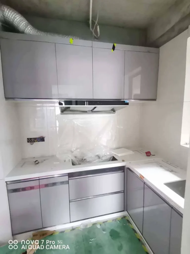 Compact L-shape kitchen cabinets with glossy gray doors and white quartz countertop
